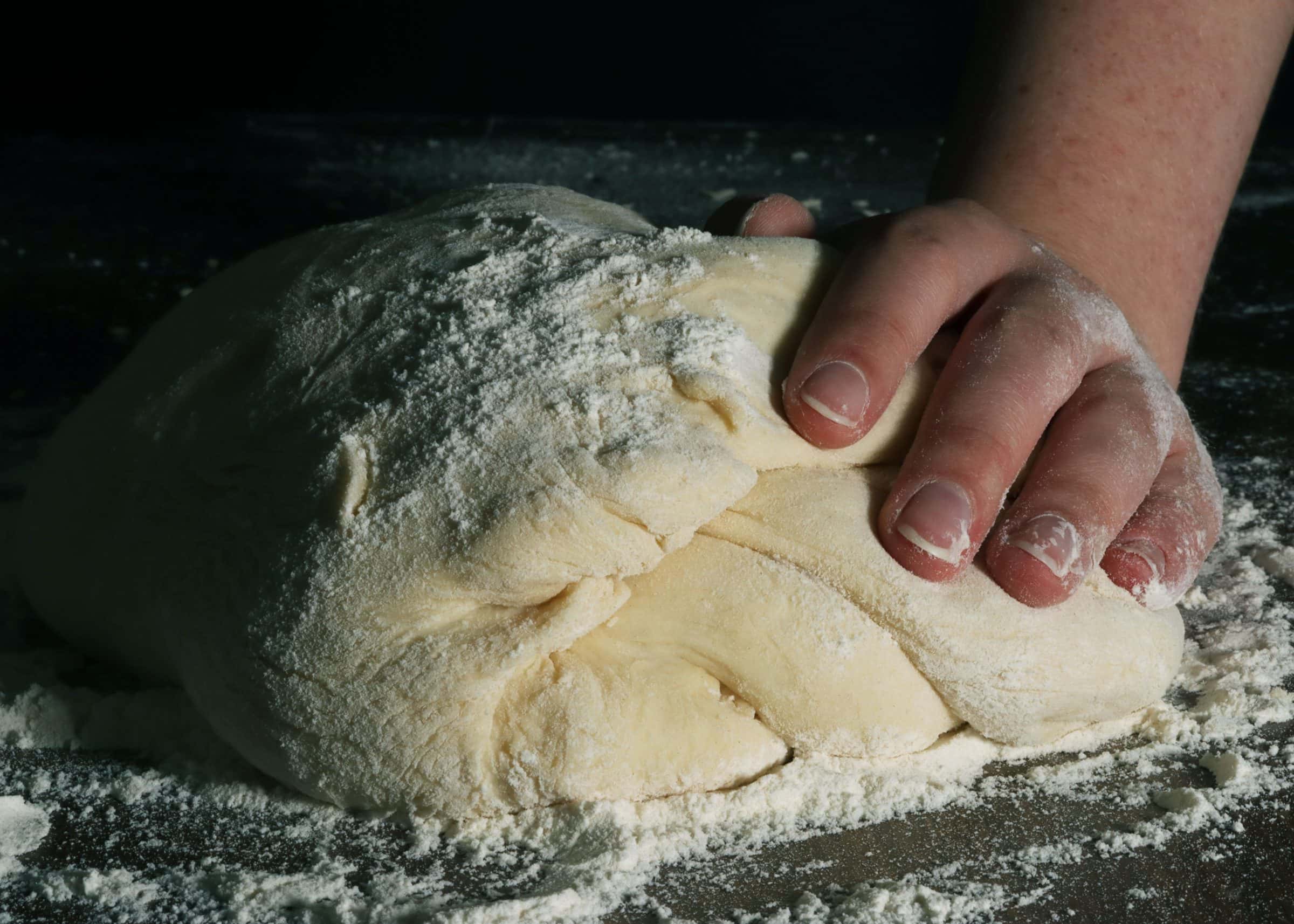 Handen kneden een meelrijke deegbal op een bakkerstafel