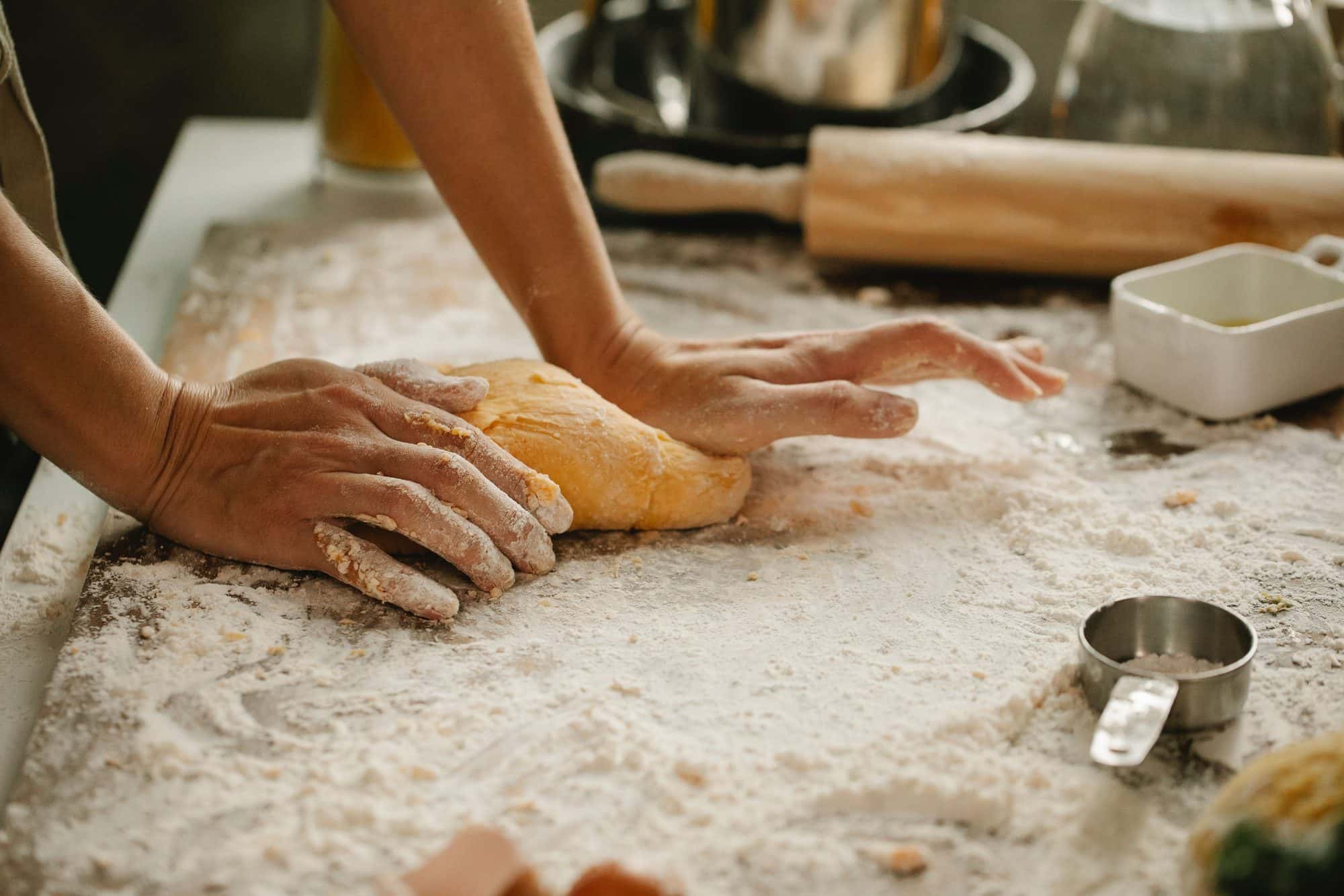 Handen kneden deeg op een met meel bestoven tafel naast een deegroller