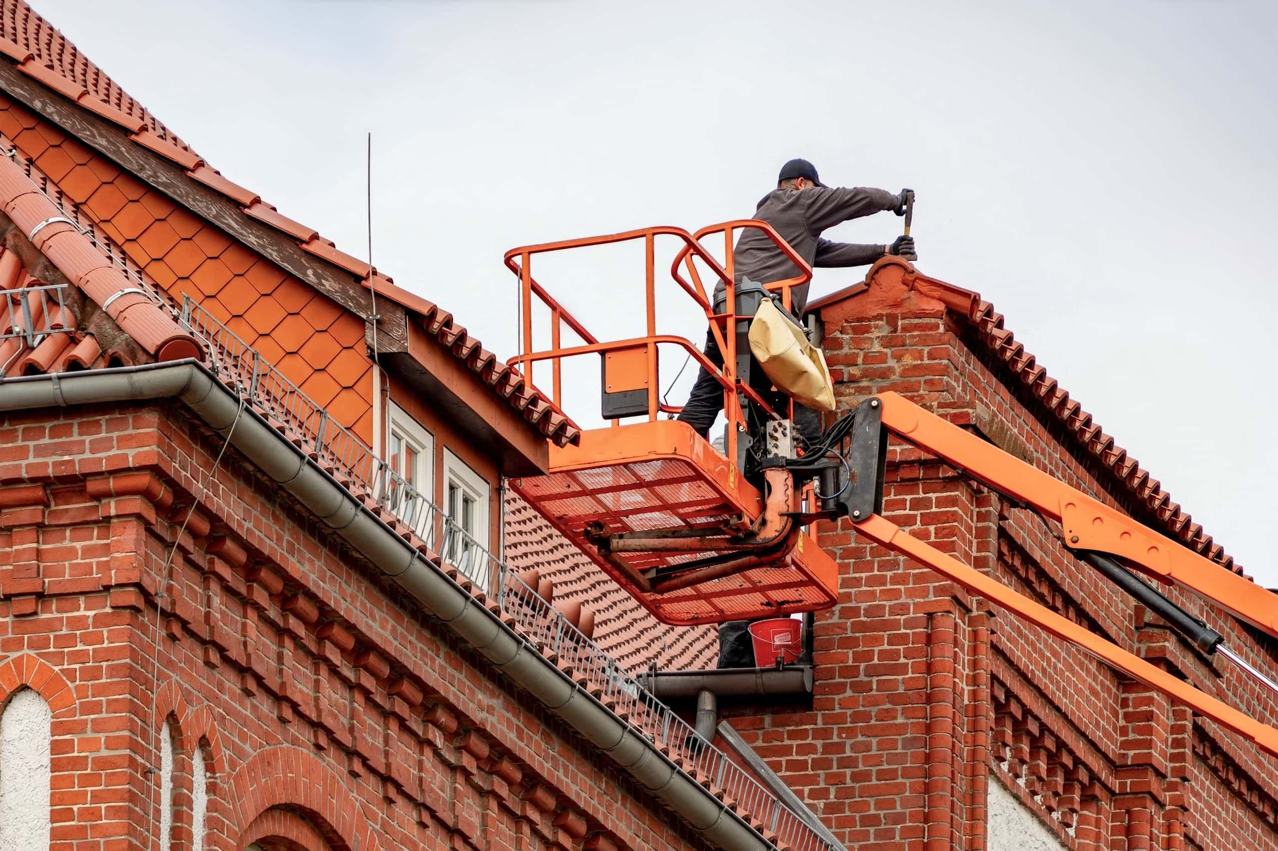 Dakdekker werkt vanaf een hoogwerker aan een dak van rode dakpannen en baksteen
