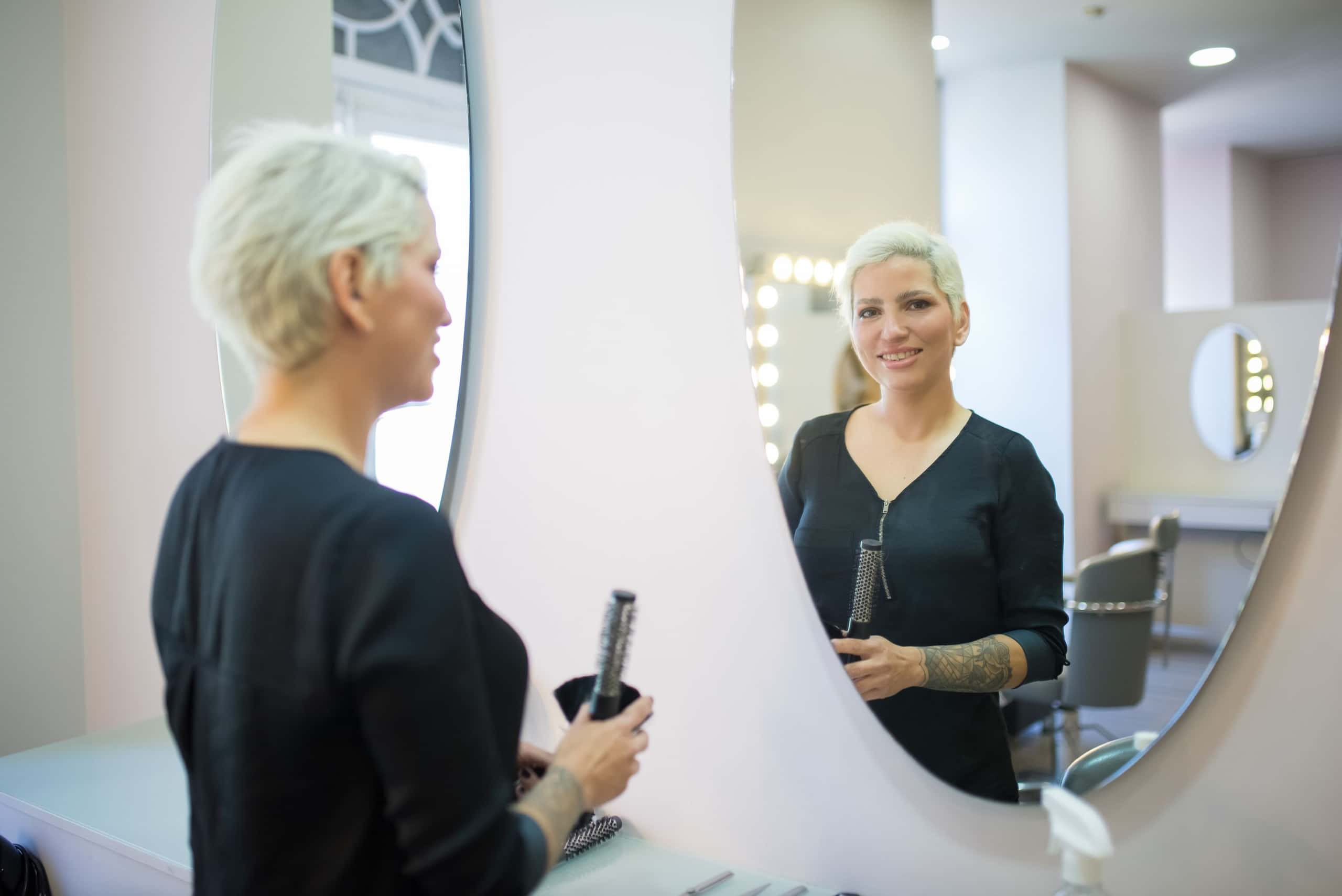 Stylist met een haartang kijkt in de ronde spiegel van de salon