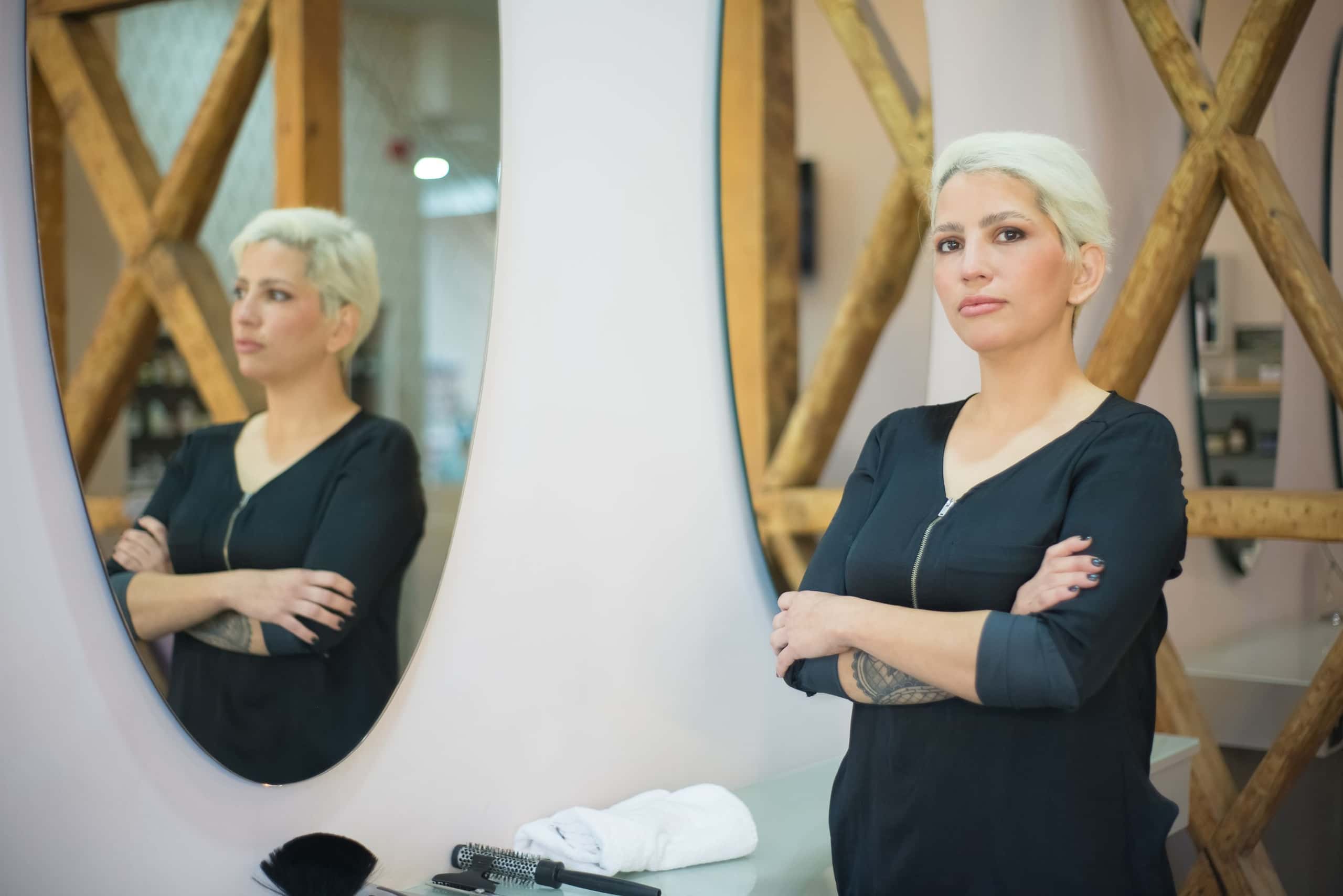 Stylist staat met gekruiste armen voor de ronde spiegels van de salon