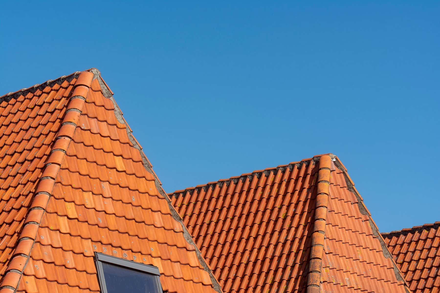 Rode dakpannen van een pannendak tegen een heldere blauwe lucht