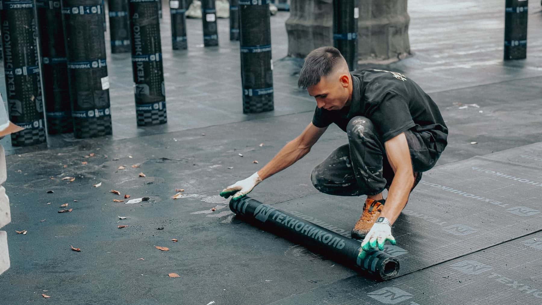 Dakdekker rolt een bitumen dakbaan uit op een plat dak