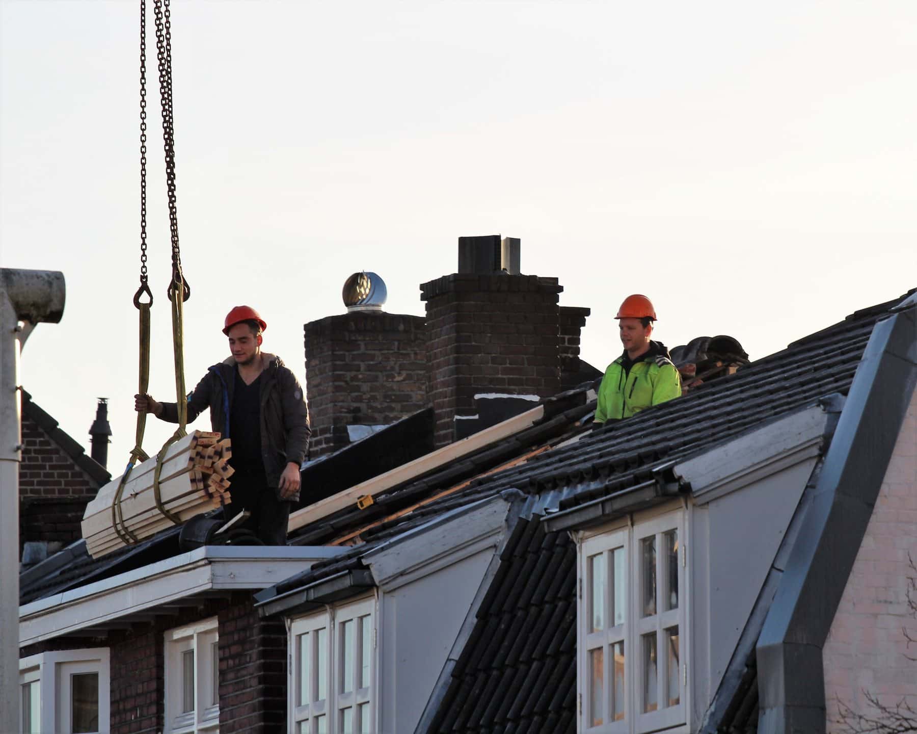 Dakdekkers werken aan een dak terwijl materiaal met een kraan omhoog wordt gehesen