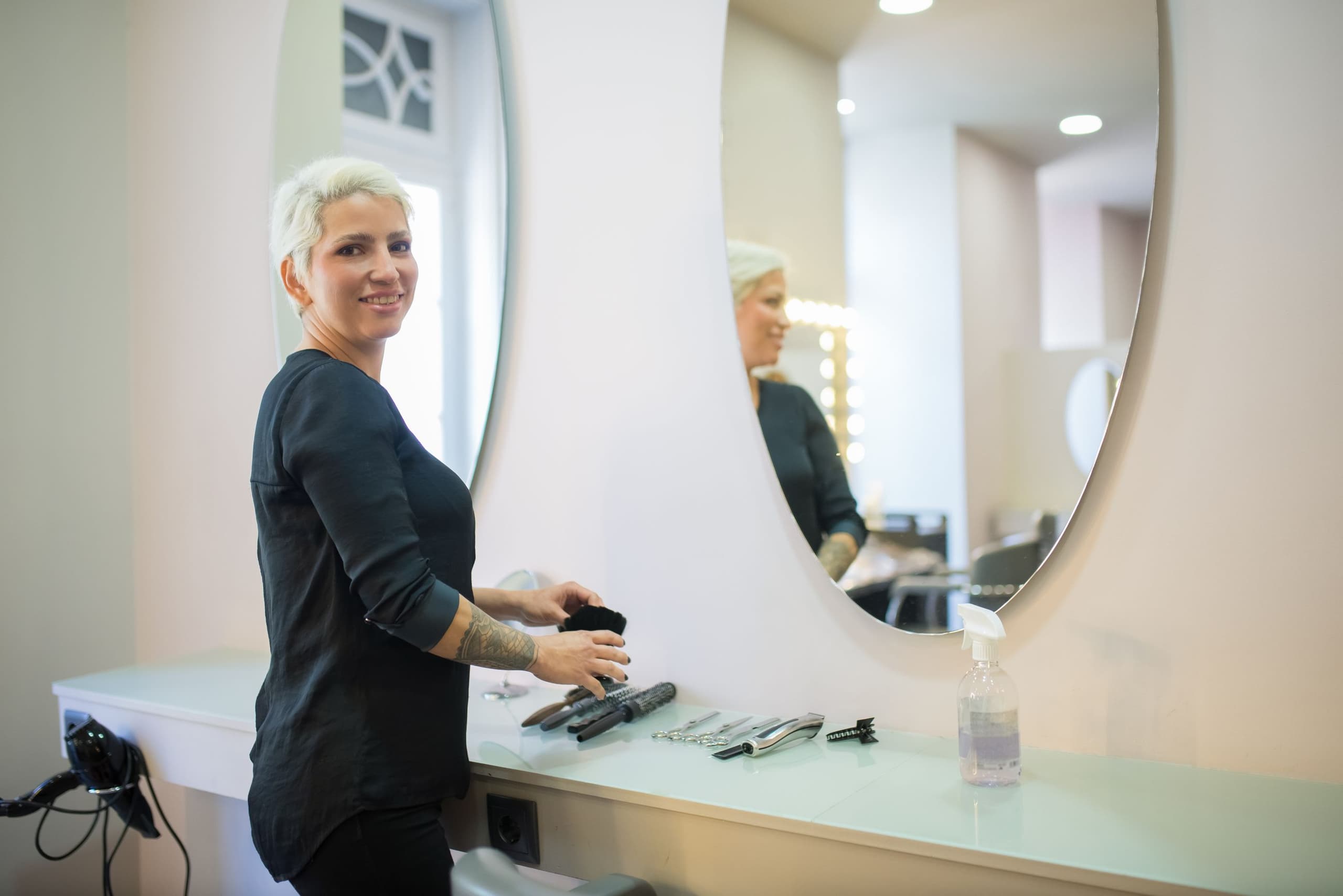 Stylist staat bij haar spiegel en werkplek in de salon