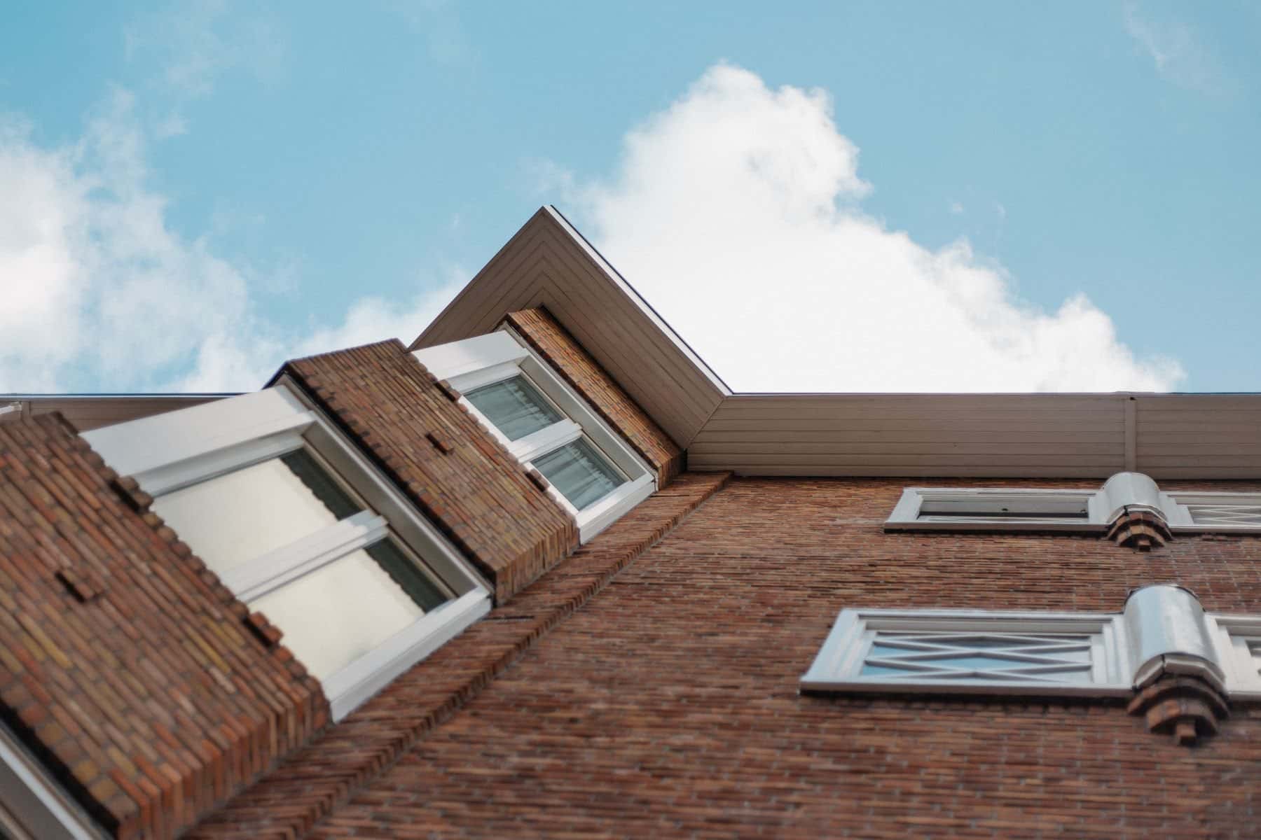 Dakkapel in een bakstenen woning onder een blauwe lucht