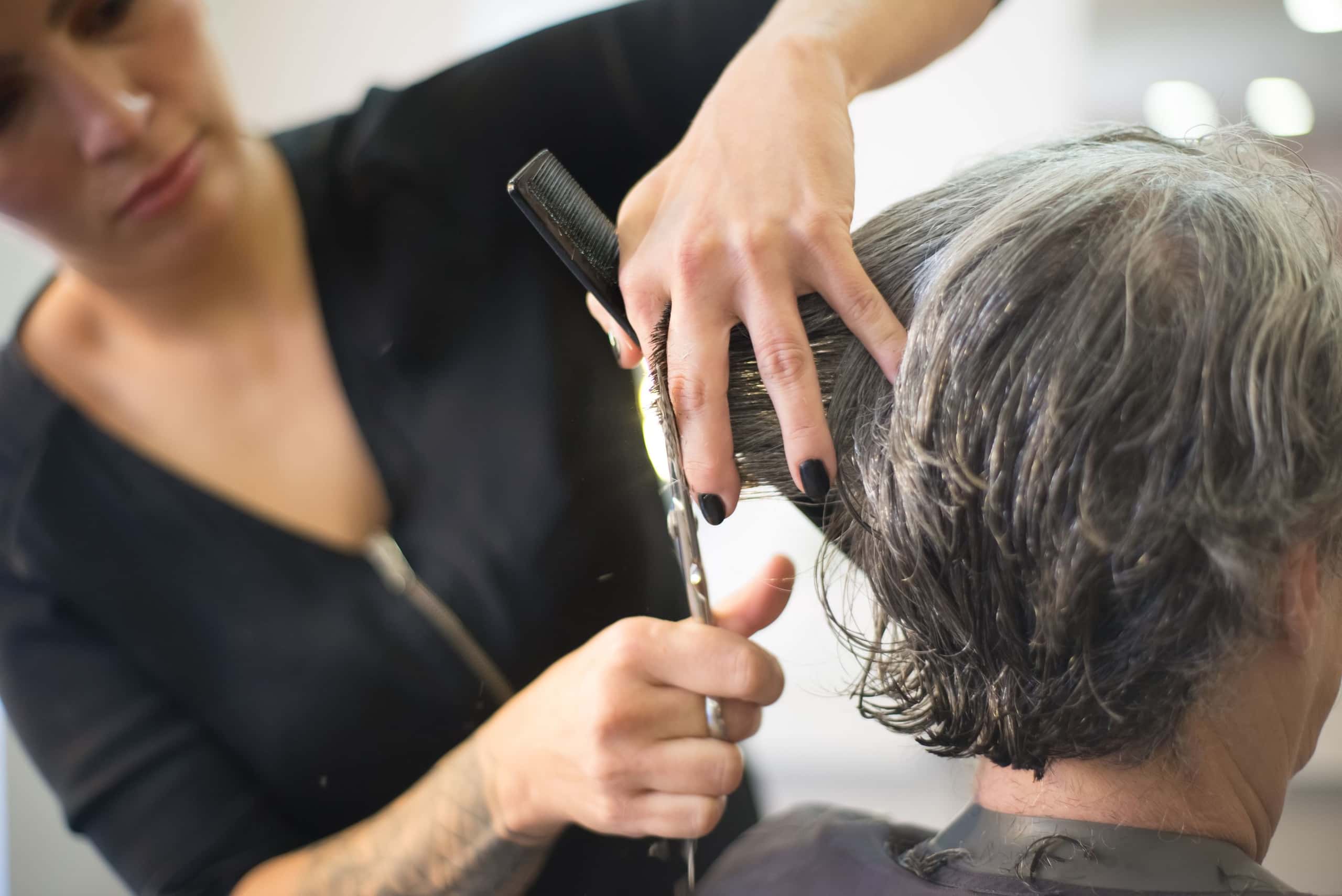 Stylist knipt met een schaar en kam het haar in de nek van een klant