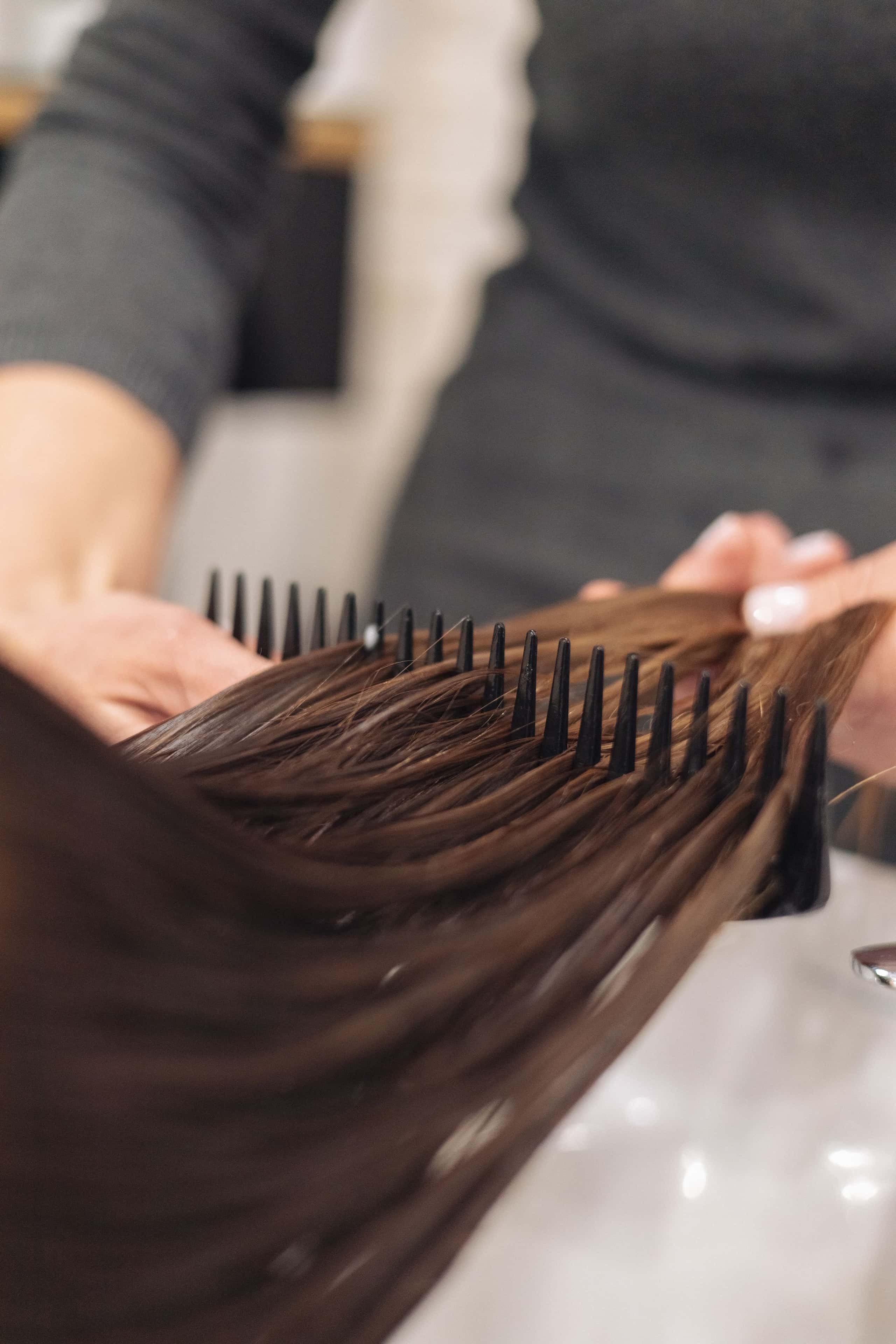 Handen kammen lang donkerbruin haar tijdens een kleurbehandeling