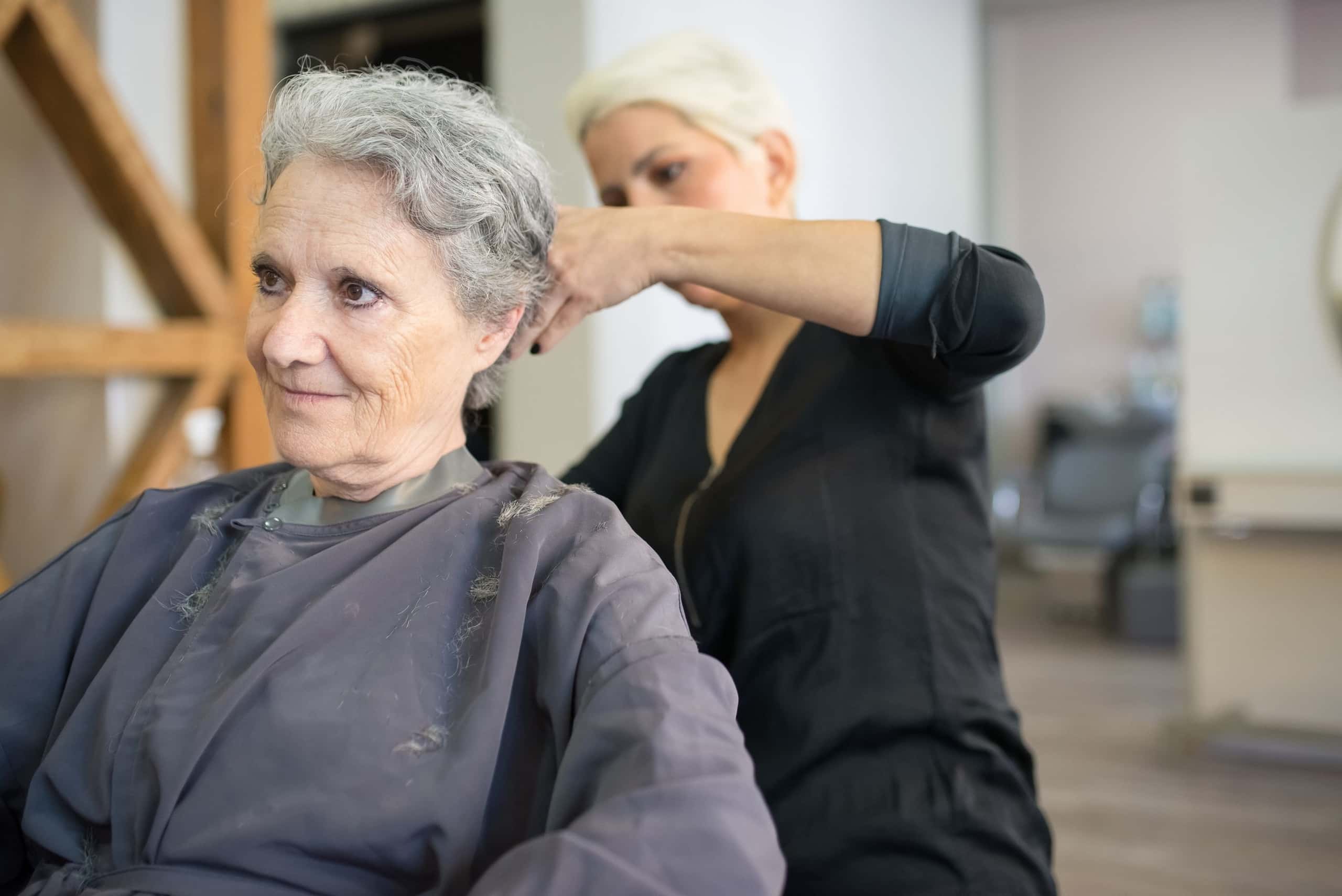 Klant lacht naar de stylist die haar haar knipt in een lichte salon met houten kruis