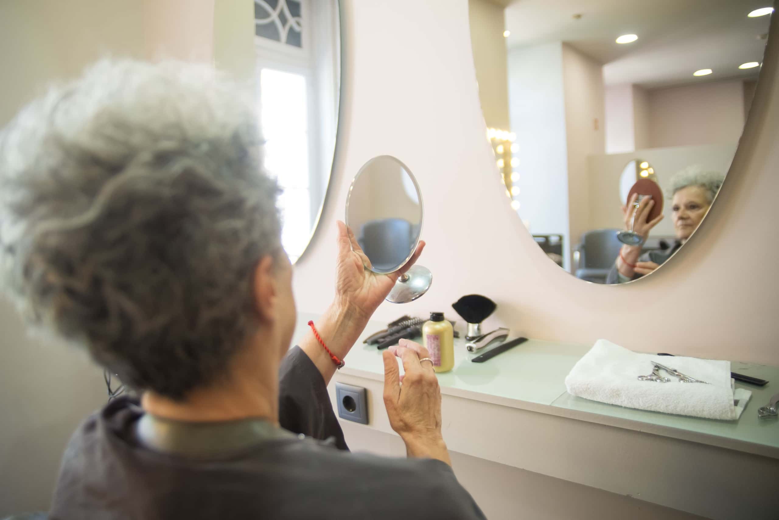 Klant houdt een handspiegel vast en kijkt naar haar nieuwe kapsel voor een ronde spiegel