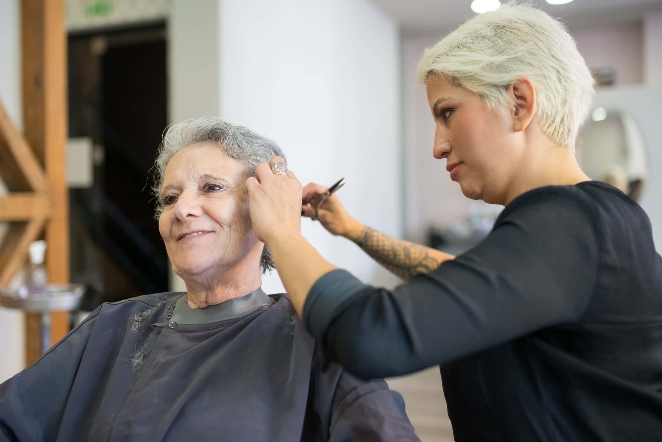 Lachende klant tijdens het knippen, met de stylist achter haar in de salon